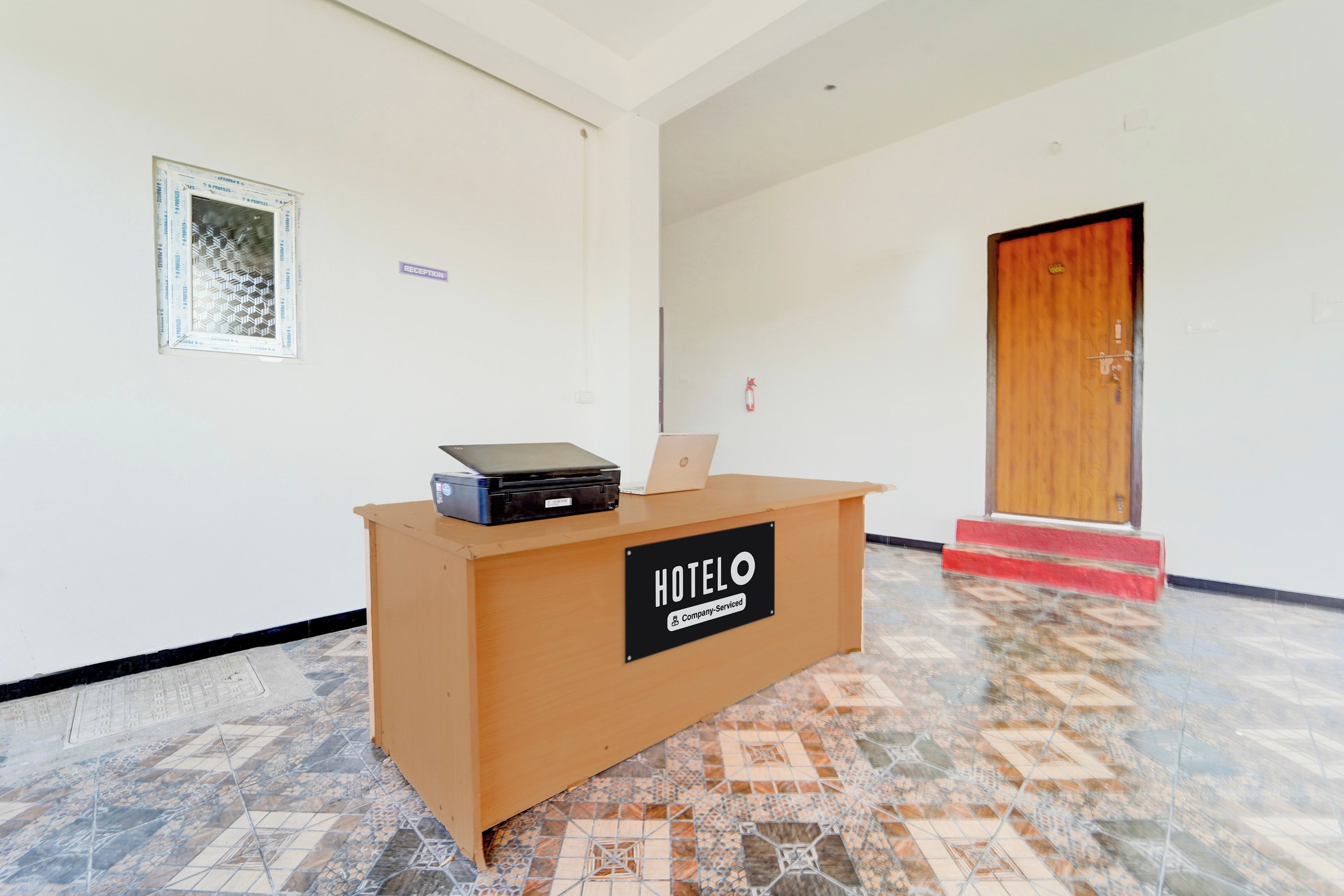 A reception desk with a sign indicating it's company-serviced, a fire extinguisher, and a wooden door in the background.