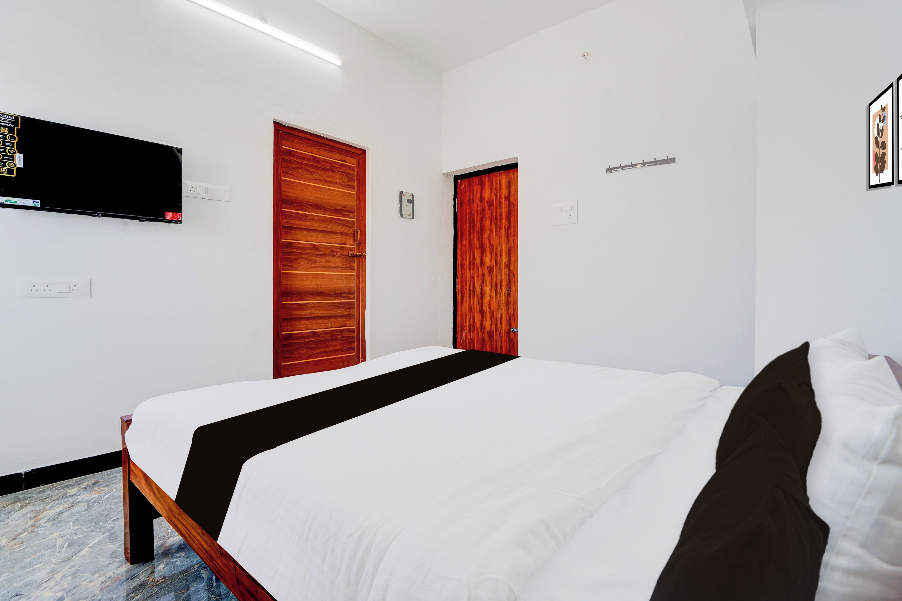 A hotel room with a bed, two doors, a flat-screen TV mounted on the wall, and a power outlet.