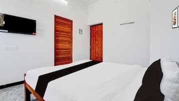 A hotel room with a bed, two doors, a flat-screen TV mounted on the wall, and a power outlet.