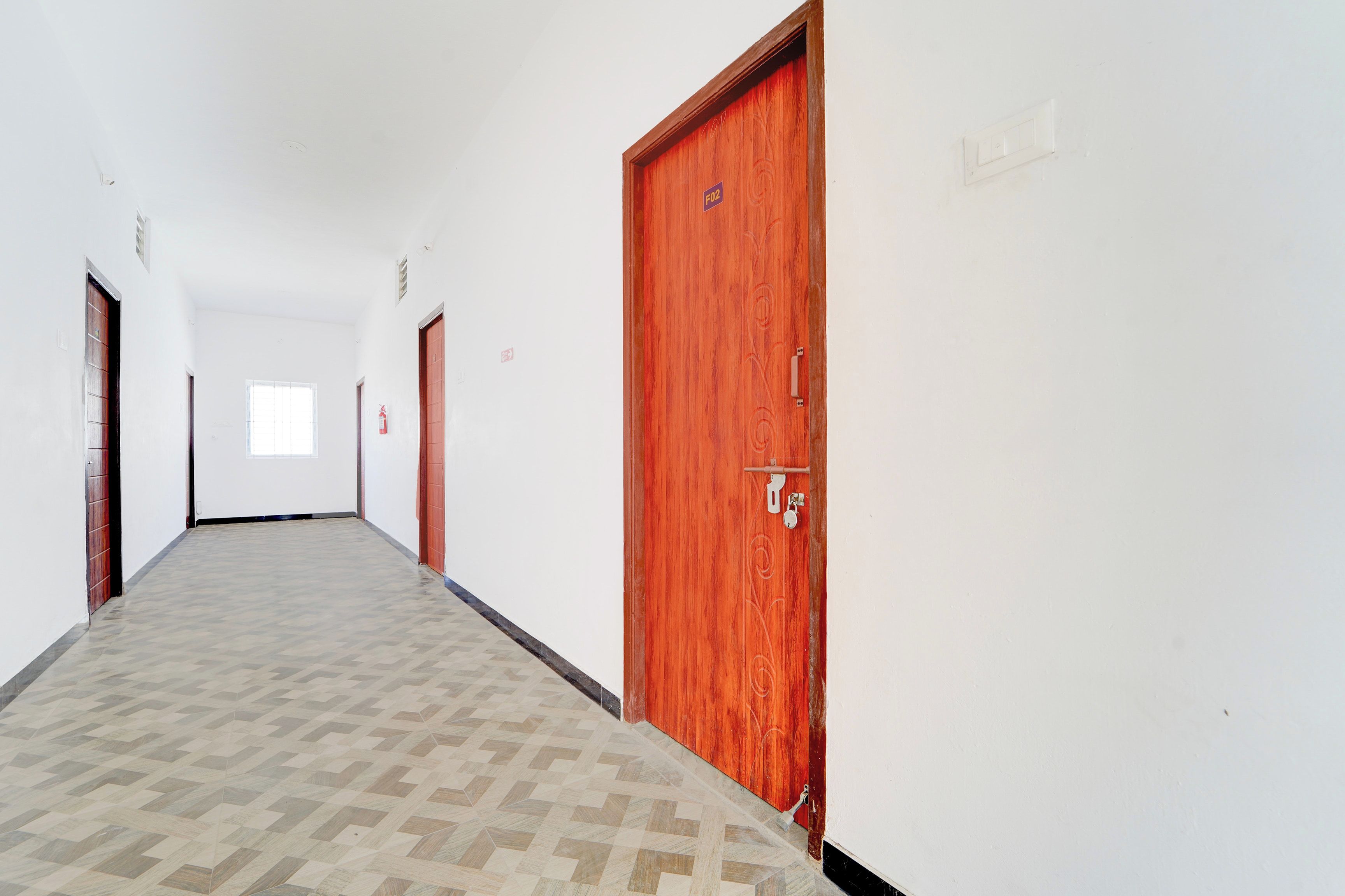 Un pasillo con piso estampado, puertas de madera y un extintor en la pared.