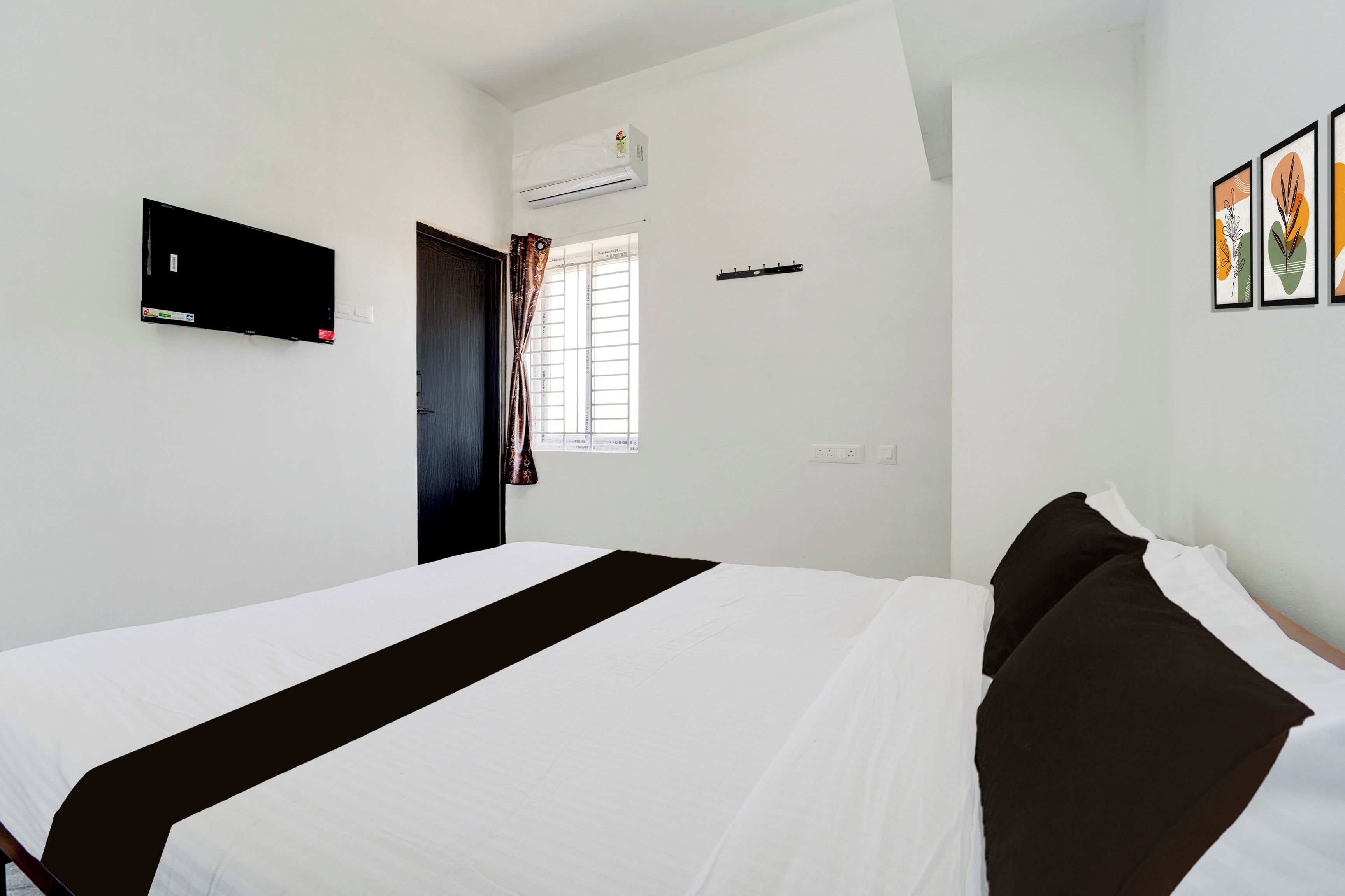 Habitación de hotel con cama, televisor de pantalla plana, equipo de aire acondicionado, ventana con cortinas y toma de corriente en la pared.