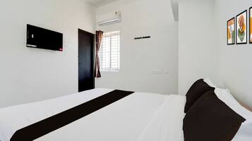 Habitación de hotel con cama, televisor de pantalla plana, equipo de aire acondicionado, ventana con cortinas y toma de corriente en la pared.