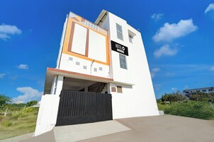 A modern hotel with a white facade, a black entrance gate, and a sign indicating it is a company service hotel.
