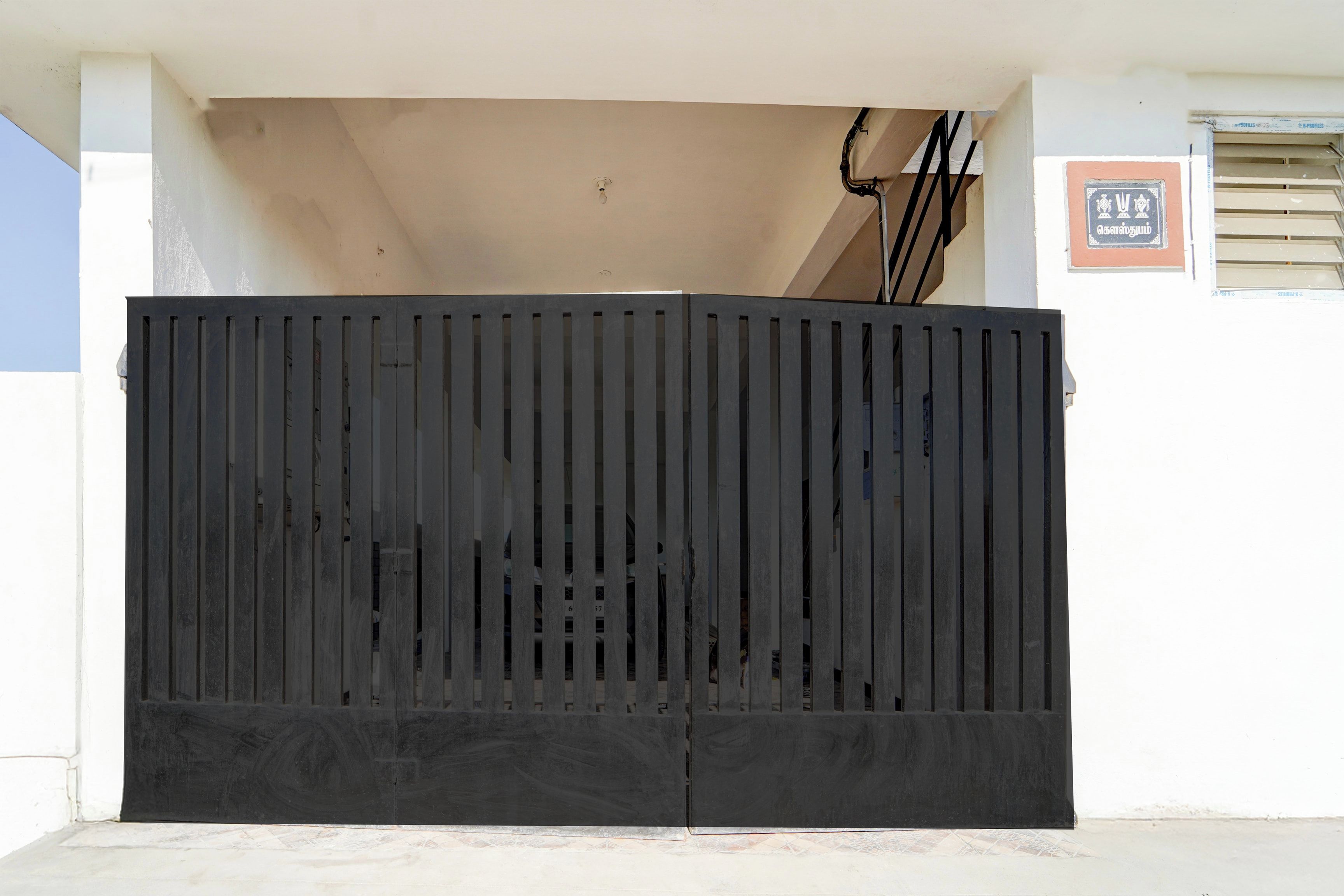 A black metal gate with vertical slats, a beige wall, and a small sign with text.