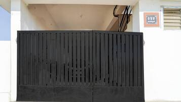A black metal gate with vertical slats, a beige wall, and a small sign with text.