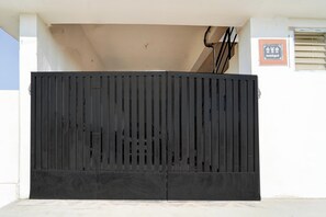 Um portão de metal preto com ripas verticais, uma parede bege e uma pequena placa com texto.