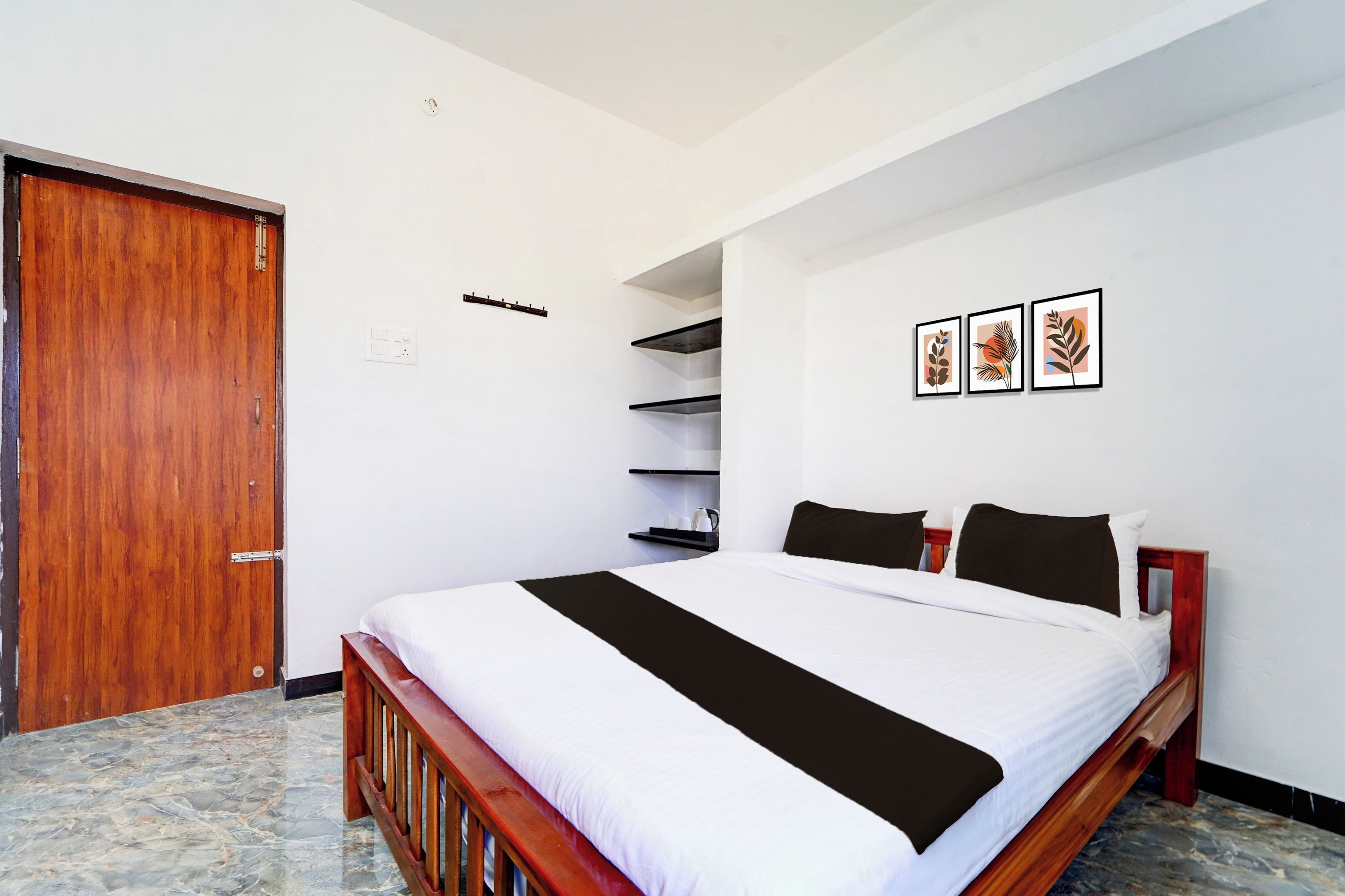 Une chambre d’hôtel avec un lit en bois, du linge de lit blanc, une armoire en bois, une étagère et trois œuvres d’art encadrées accrochées au mur.