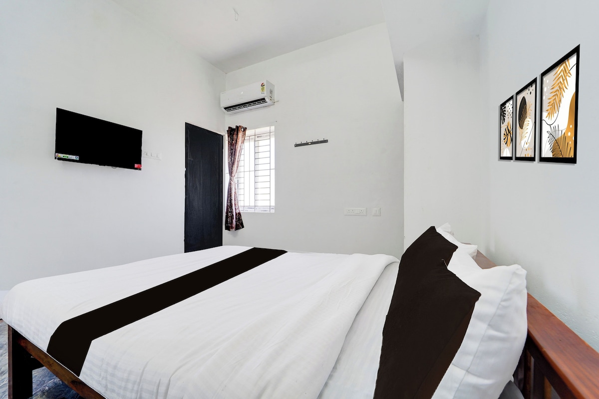 Quarto de hotel com uma cama, televisão de tela plana, aparelho de ar condicionado, janela com cortinas e arte emoldurada na parede.
