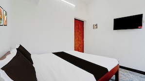 Hotellihuone, jossa on sänky, seinälle asennettu televisio ja ovi.