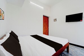 Quarto de hotel com cama, televisão fixada na parede e porta.