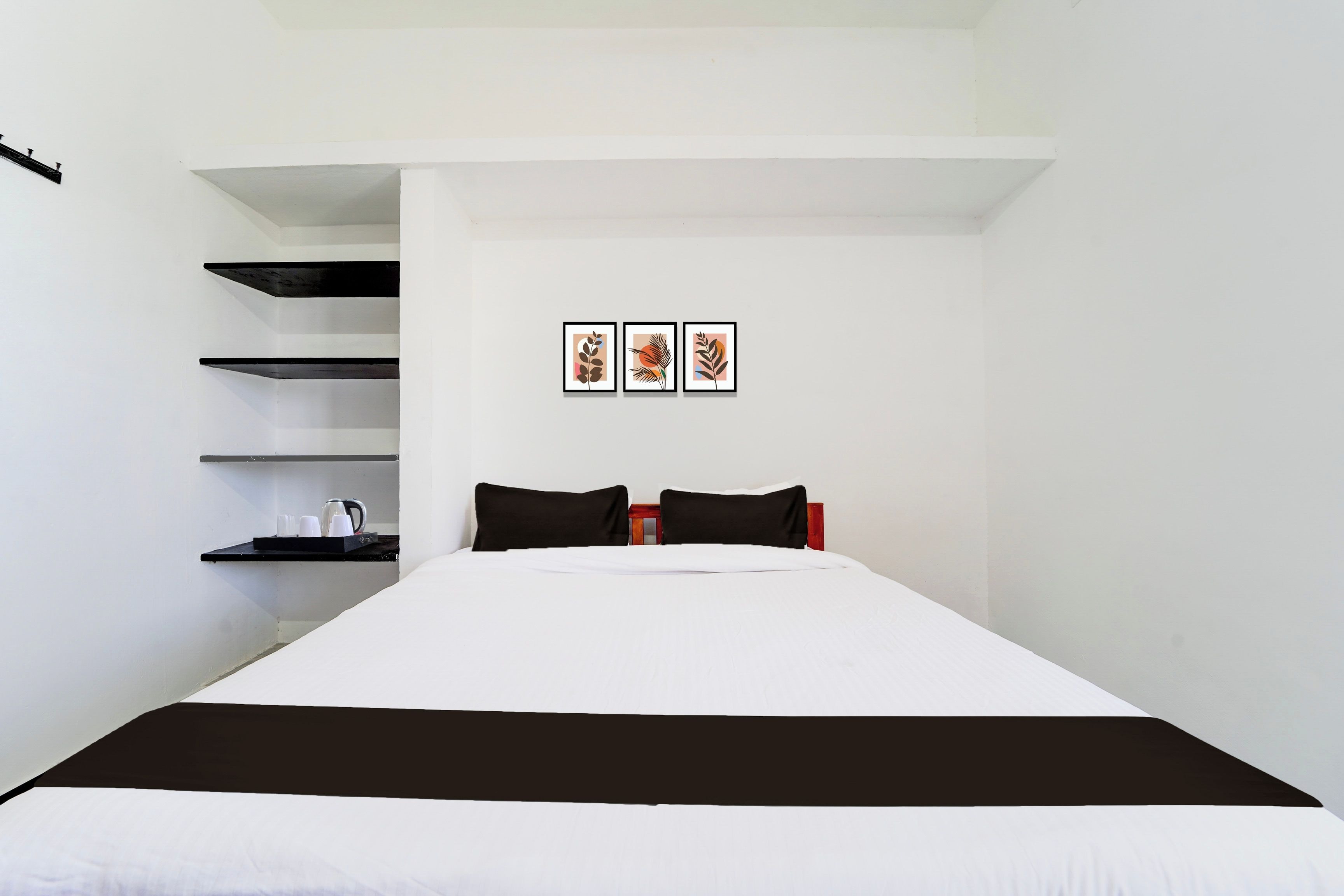 Une chambre à coucher avec un lit, une literie noire et blanche, une étagère avec une bouilloire et des tasses, et trois tableaux encadrés accrochés au mur.