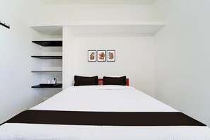 A bedroom with a bed, black and white bedding, a shelf with a kettle and cups, and three framed pictures on the wall.