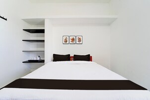 A bedroom with a bed, black and white bedding, a shelf with a kettle and cups, and three framed pictures on the wall.