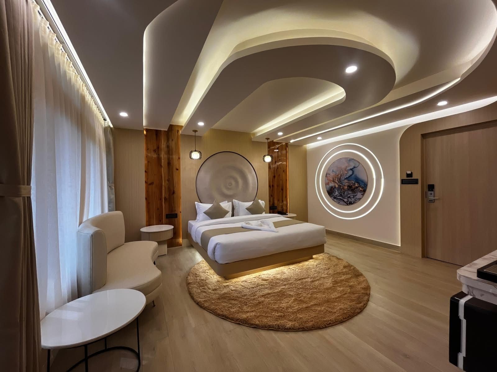 Une chambre d’hôtel moderne avec un grand lit, un tapis rond, une table ronde et un mur agrémenté d’un luminaire circulaire.