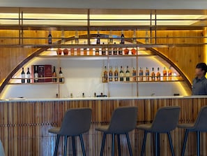 A bar area with a wooden interior, a counter with bottles, and three bar stools.