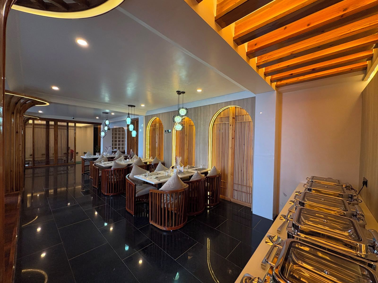 Un intérieur de restaurant moderne avec des carreaux noirs au sol, des meubles en bois et un espace buffet doté de plateaux de service en métal.