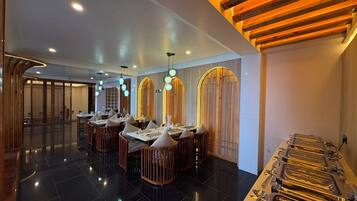 A modern restaurant interior with black-tiled floors, wooden furniture, and a buffet area with metal serving trays.