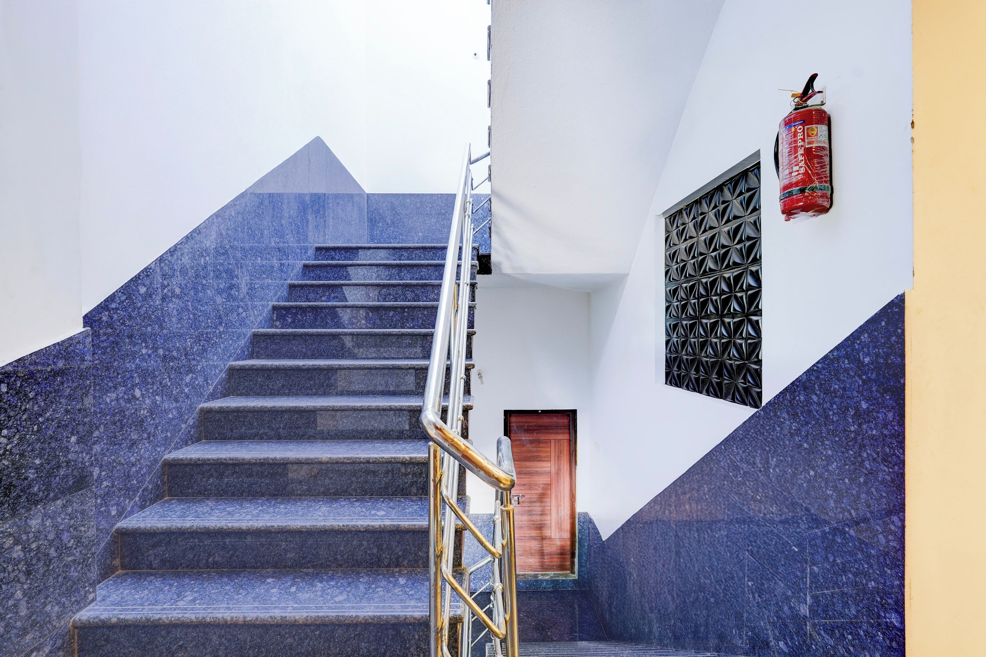 Un escalier menant à une porte en bois, avec un extincteur fixé au mur.