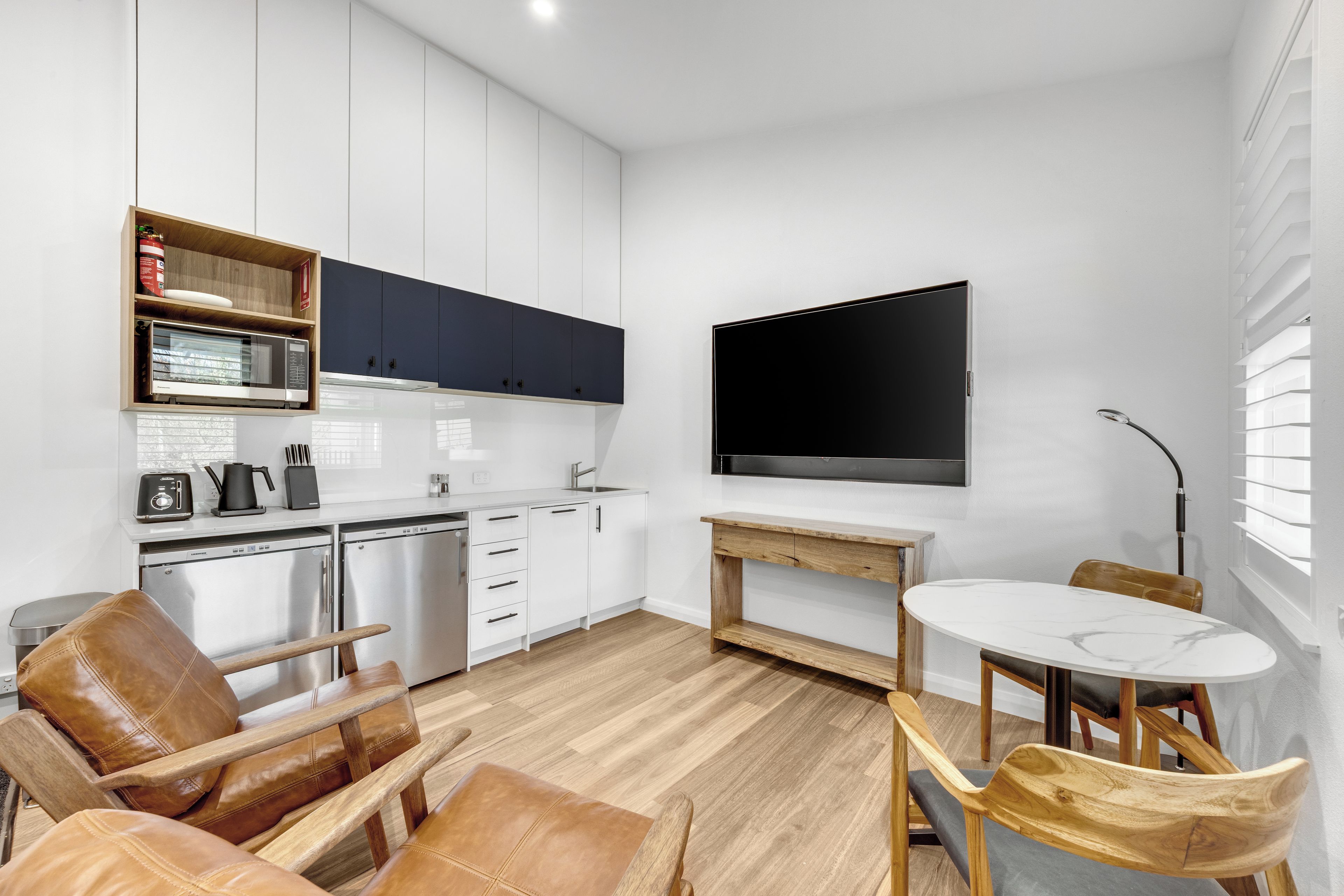 Een moderne keuken met witte kasten, een ingebouwde magnetron en een grote flatscreen televisie aan de muur.