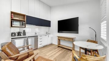 A modern kitchen with white cabinets, a built-in microwave, and a large flat-screen TV mounted on the wall.