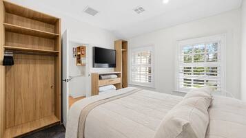 A bedroom with a bed, a TV, a wardrobe, and a window with blinds.