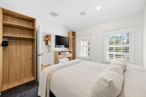 Un dormitorio con cama, televisor, armario y ventana con persianas.