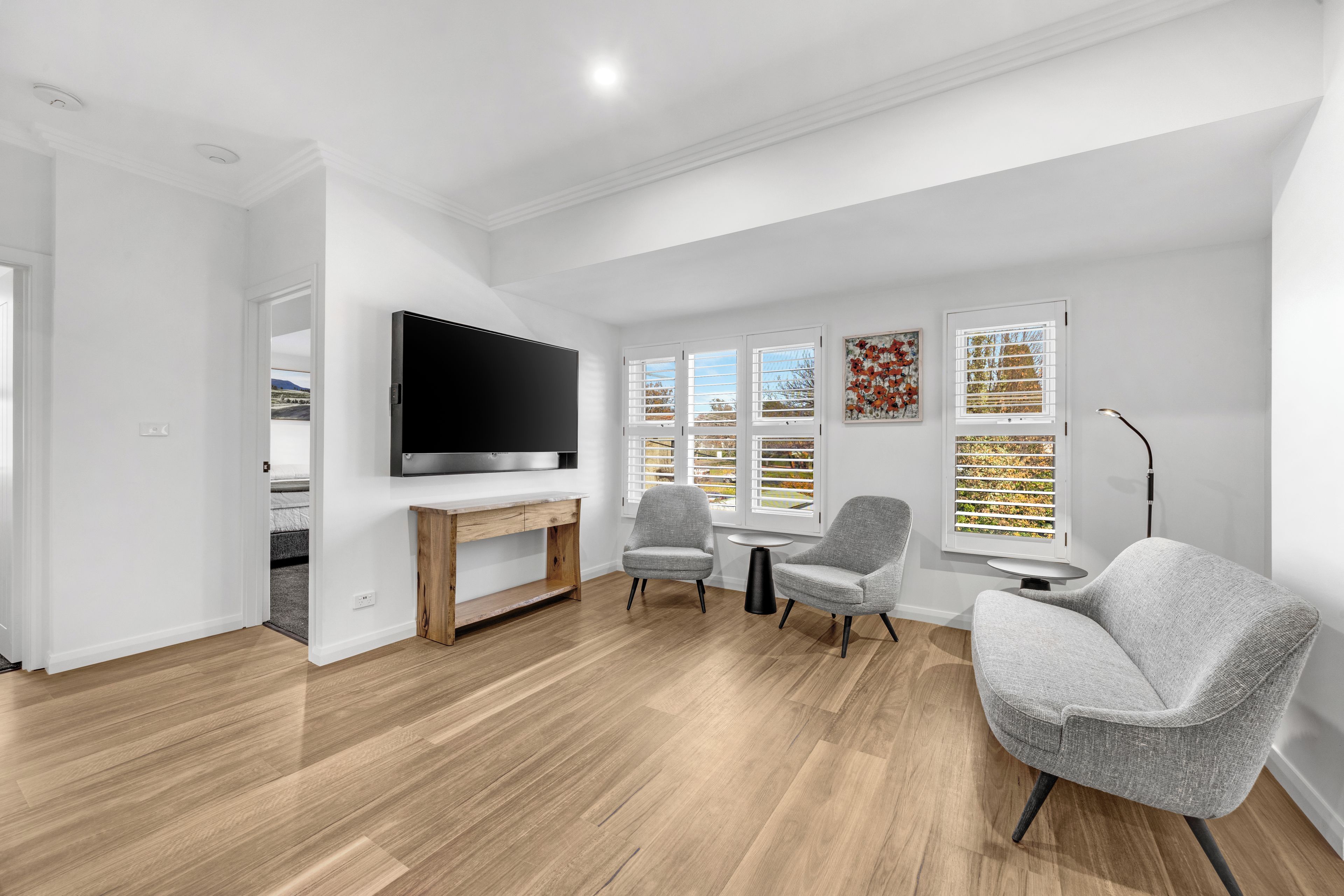 Een moderne woonkamer met een flatscreen televisie, een houten salontafel, twee grijze fauteuils en een kleine ronde tafel.
