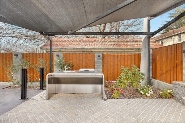 Un espacio al aire libre para barbacoa con una parrilla, una zona de estar cubierta y un patio de ladrillo.