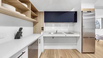 A modern kitchen with white cabinetry, a stainless steel refrigerator, and wooden shelves.