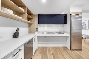A modern kitchen with white cabinetry, a stainless steel refrigerator, and wooden shelves. - Pilgrims Apartments (Griffith)