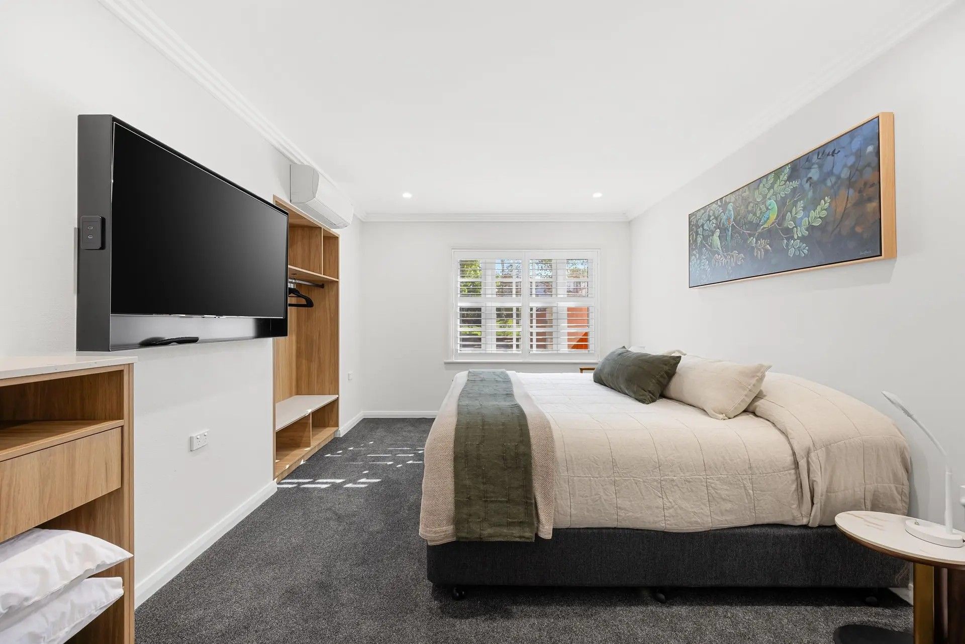A bedroom with a bed, a TV, a window, and a painting.