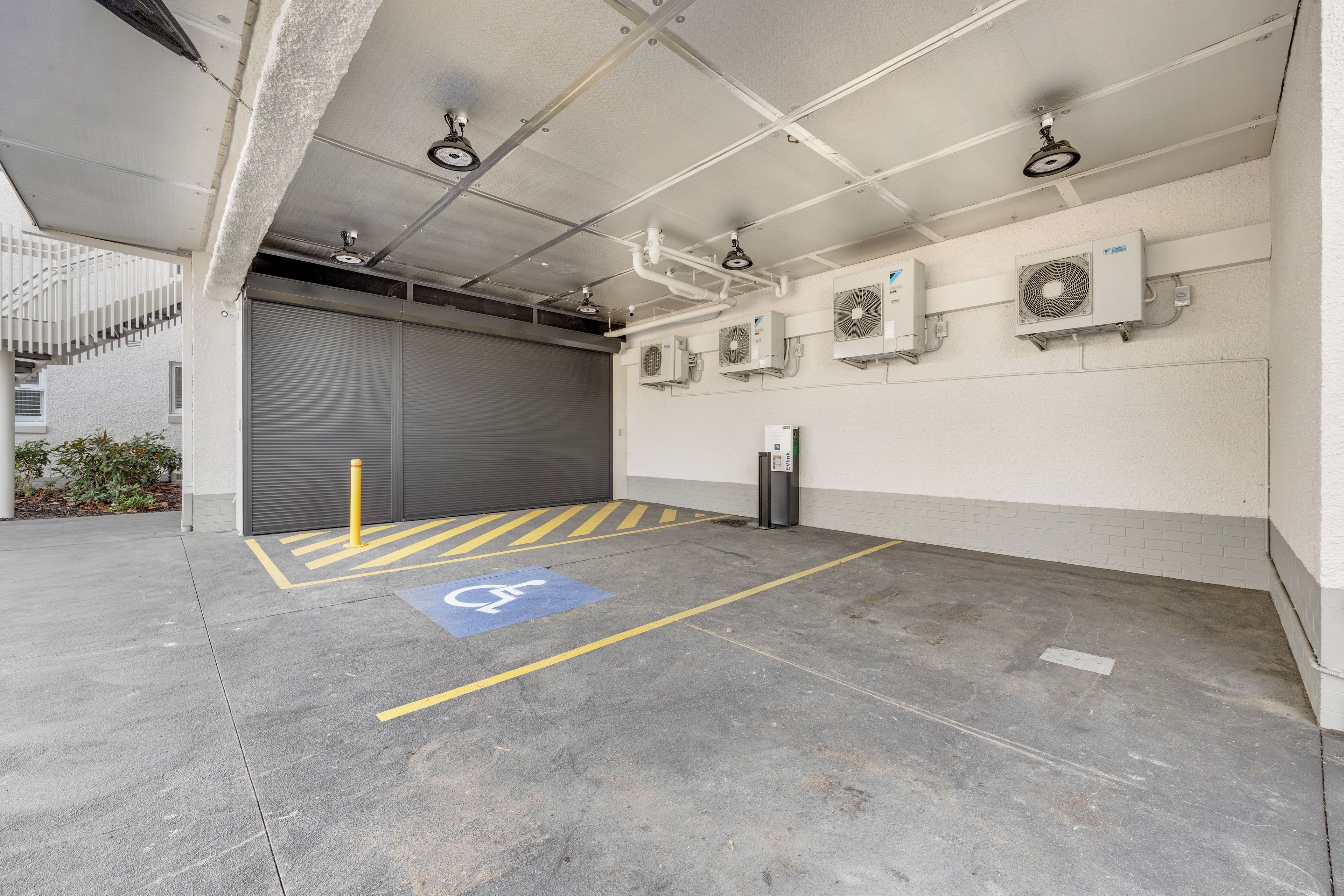 A parking garage with a disabled parking space, ventilation units, and a closed garage door.