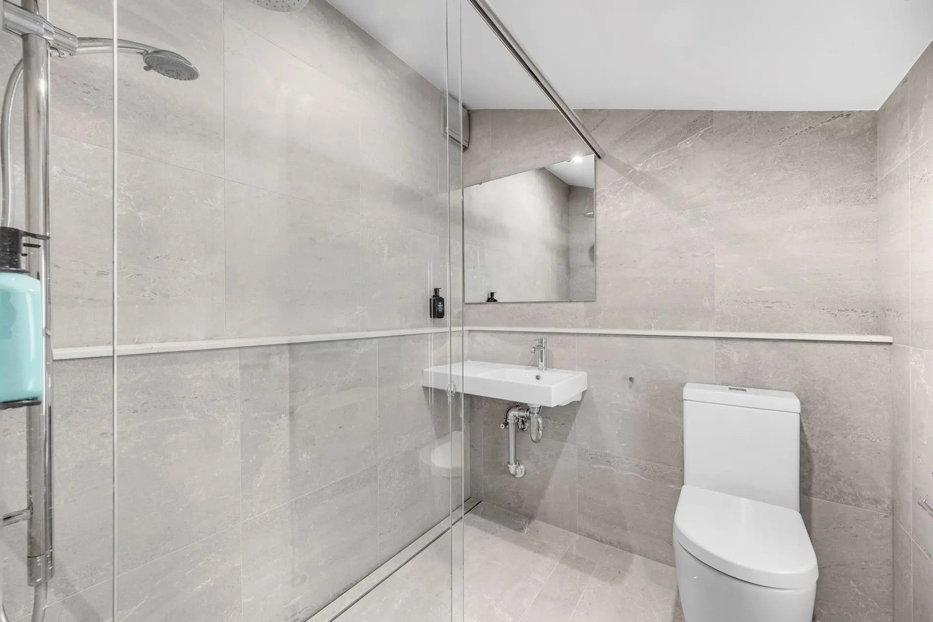 Ein modernes Badezimmer mit einer gläsernen Dusche, einem weißen Waschbecken und einer Toilette.