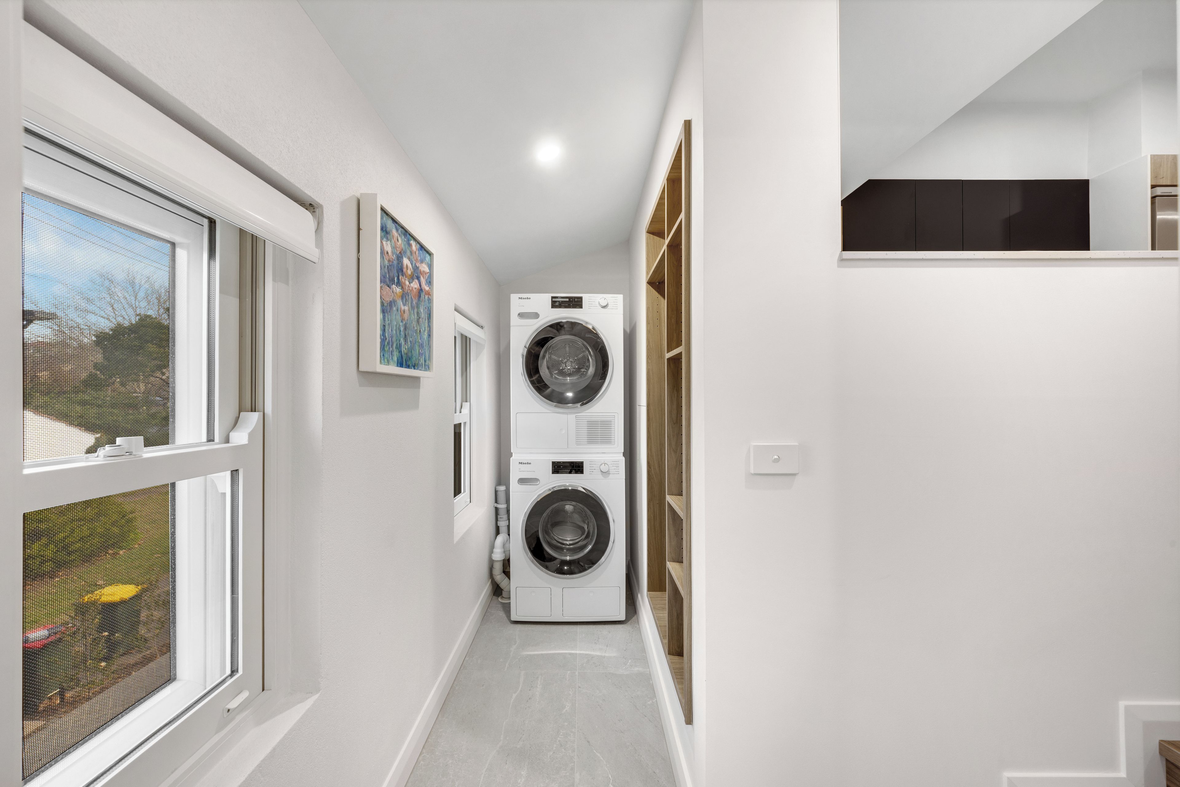 Un lavadero con dos lavadoras apiladas, una ventana con vistas al exterior y una puerta que da a otra habitación.