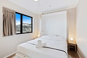 Ein Hotelzimmer mit Bett, Fenster mit Vorhängen, Nachttisch mit Lampe und Blick auf die Stadt.