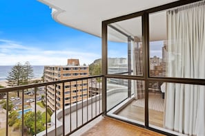 Ein Balkon mit Blick auf einen Strand und Gebäude, mit Fliesenboden und Geländer.