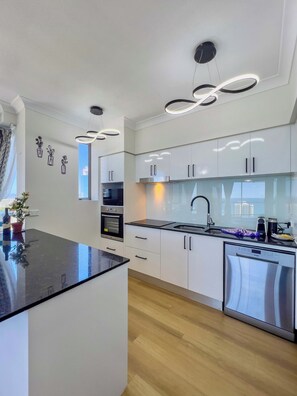 Cozinha moderna com armários brancos, eletrodomésticos de aço inoxidável e bancada preta.