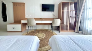 Hotellihuone, jossa on sänky, työpöytä, kaksi tuolia, televisio, vaatekaappi ja ilmastointilaite.