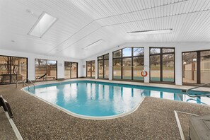 An indoor swimming pool with clear glass walls, a pebble floor, and a view of the outside. - Foothills Getaway 2BR Home (Branson)