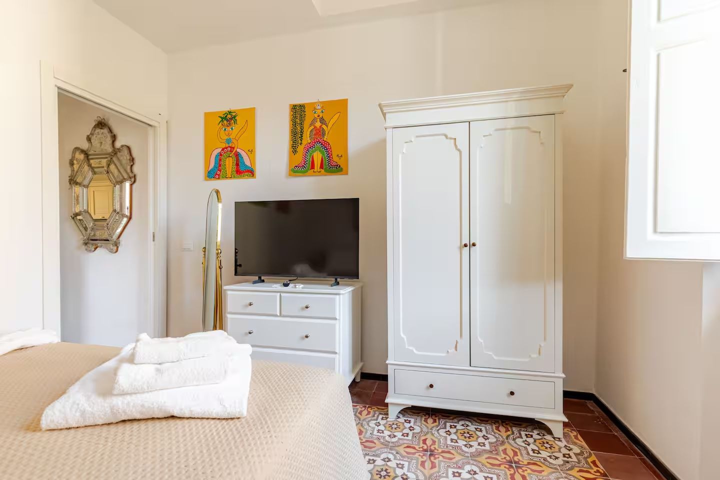 Un dormitorio con cama, un armario blanco, una televisión y dos cuadros colgados en la pared.