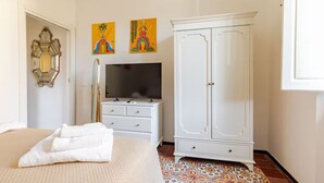 Ein Schlafzimmer mit einem Bett, einem weißen Kleiderschrank, einem Fernseher und zwei an der Wand hängenden Bildern.
