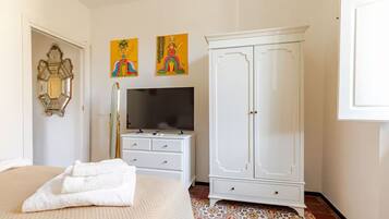 Un dormitorio con cama, un armario blanco, una televisión y dos cuadros colgados en la pared.
