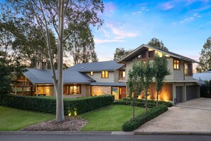 A two-story house with a covered porch, a garage, and a well-maintained lawn. - STONEWOOD - The Vintage Holiday Houses (POKOLBIN)