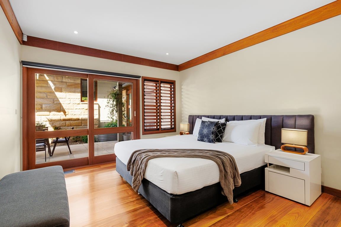 A bedroom with a large bed, a nightstand, a bench, and a sliding glass door leading to an outdoor area.