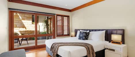 A bedroom with a large bed, a nightstand, a bench, and a sliding glass door leading to an outdoor area.