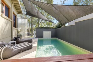 A swimming pool with a shaded area, a seating area with cushions, and a tiled floor. - STONEWOOD - The Vintage Holiday Houses (POKOLBIN)