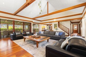 A spacious living room with a high ceiling, wooden beams, a large sofa, a coffee table, and a view of the outdoors. - STONEWOOD - The Vintage Holiday Houses (POKOLBIN)