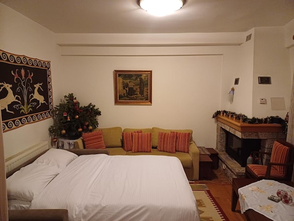 A cozy room with a bed, a sofa, a fireplace, and a Christmas tree.
