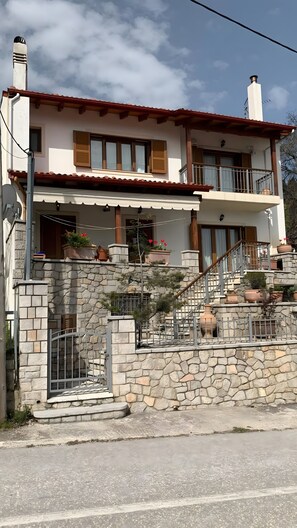 Una casa de dos pisos con fachada de piedra, contraventanas de madera y un balcón con macetas.