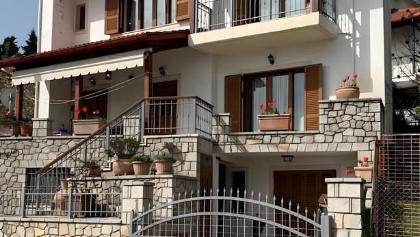 Ein zweigeschossiges Haus mit einer Steinfassade, einem Metallgitter und einem Balkon mit Geländer.